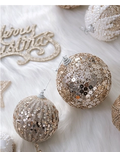 Close-up of champagne gold sequined and striped Christmas balls on white plush fabric