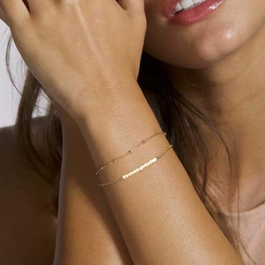 Detail showing layered gold chain bracelets with pearls on a female model's wrist