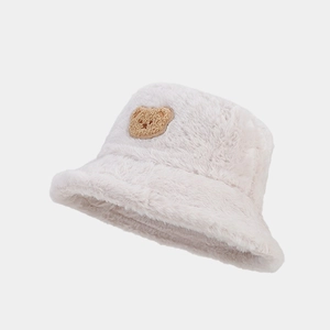 Detail of soft cream plush bucket hat featuring a brown teddy bear patch and fuzzy texture