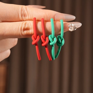 Detailed view of matte red and green knotted earrings held to show smooth texture