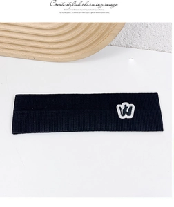 Detail of black ribbed knit sports headband featuring a white embroidered W letter patch
