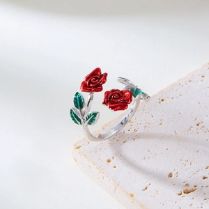 Close-up of red rose enamel flower ring with green leaves on beige stone texture