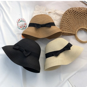 Flat lay of colorful straw sun hats with black ribbons and matching woven handbag