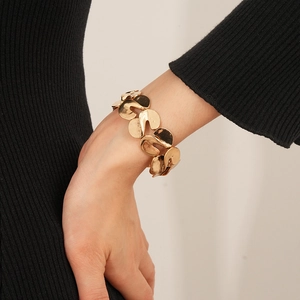 Detail of a gold wavy S-shaped metal bracelet worn on a wrist over black fabric