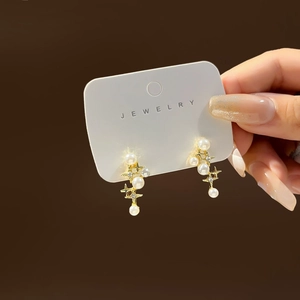Elegant gold star earrings with pearls and zircon crystals shown on a jewelry card