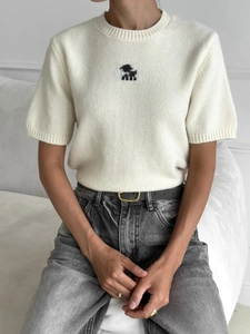 Dettaglio di top in maglia crema a maniche corte con ricamo di piccoli animali