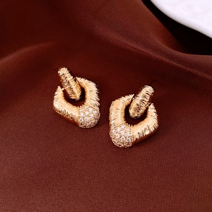 Macro shot of gold textured diamond pattern earrings with zircon inlay on silk background