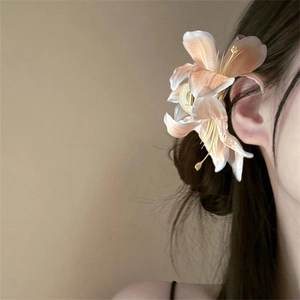 Detail of elegant orange-pink lily flower hair claw clip on model's hair with soft lighting