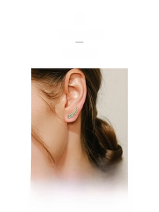 Macro detail of leaf-shaped ear climber in gold with green enamel accents on the ear