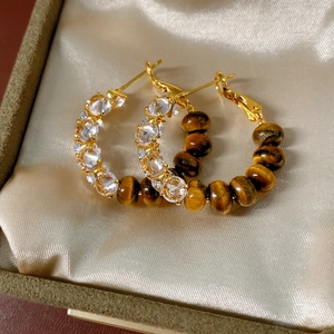 Macro detail of gold hoop earrings with sparkling zircon and tiger eye beads