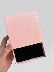 Pink drawer-style jewelry box with gold logo and soft black velvet interior lining