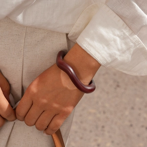 Detail of a dark brownish-red wavy acrylic bracelet on a wrist with natural lighting