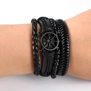 Detail of layered leather punk bracelet featuring a black nautical helm charm on wrist