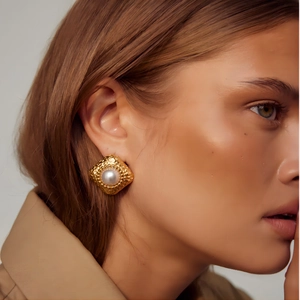 Détail de boucles d'oreilles dorées texturées avec perle blanche portées par un mannequin