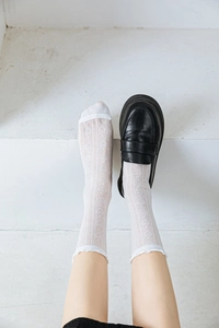 Detail of white mesh socks with ruffled cuffs worn with black leather loafers on stairs