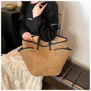 Detail showing the brown woven straw texture and premium black leather strap of the bag
