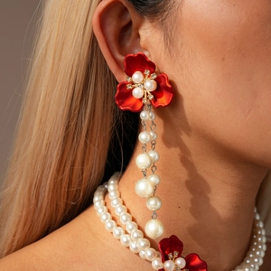 Detailed close-up of red flower earrings with pearl tassels worn by a model