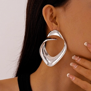 Close-up of oversized irregular geometric silver earrings with a glossy metallic finish