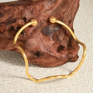 Polished 18k gold wave open bangle with sphere ends displayed on natural wood element