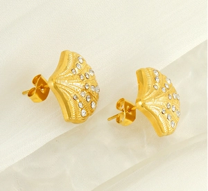 Macro view of gold shell earrings with pavé zircons and butterfly backs on white fabric