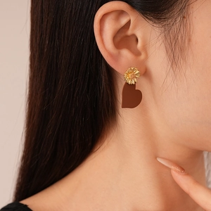 Detail shot of daisy stud earrings with heart charms on model ear in close-up view