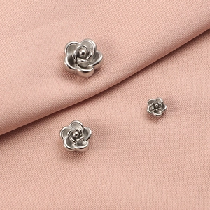 Three sizes of 3D rose-shaped stainless steel metal beads on a pink fabric background