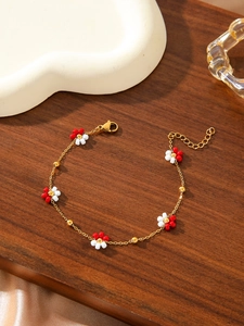 Macro shot of 18K gold-plated flower bracelet with red and white beads on wooden table