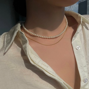 Detail of layered jewelry featuring white round pearls and a fine gold chain necklace