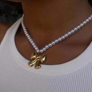 Elegant pearl necklace with oversized gold bow pendant worn by a model in soft light