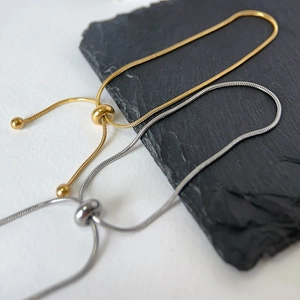 Adjustable gold and silver snake chain bracelets with slider bead on a grey stone base