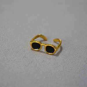 Detailed macro view of creative gold-plated sunglasses shaped ring on grey fabric texture