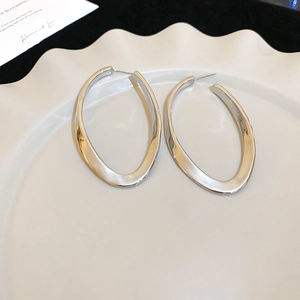 Detail of silver twisted oval hoop earrings on a white decorative ceramic plate
