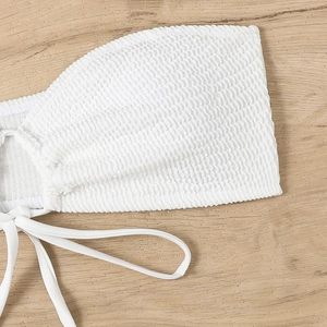 Close-up of white smocked texture bikini top with adjustable tie straps on wood background