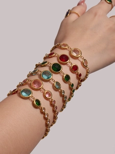 Macro view of stacked bracelets featuring colorful glass gems and gold plated steel chains