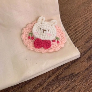 Detailed macro view of a handmade crochet rabbit brooch with red bow and cherry details