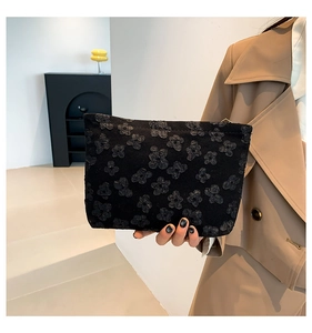 Detail of a black floral embossed clutch bag with metal zipper held by a model