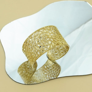 Detailed close-up of golden hollow cuff bracelet with floral patterns on a mirror surface