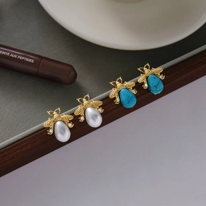 Golden bee stud earrings with pearls, turquoise, and zircons displayed on a velvet tray