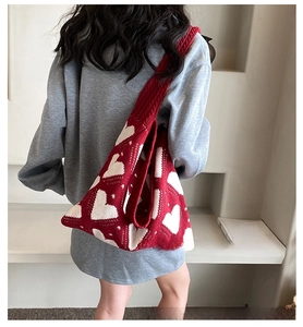 Rear view of a red knitted tote bag with white heart patterns and wide shoulder strap
