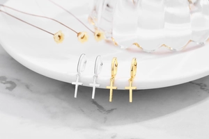 Macro shot of silver and gold cross pendant earrings displayed on a ceramic plate edge