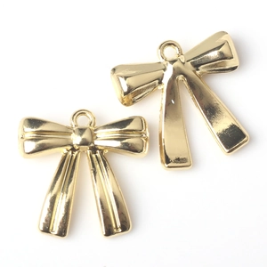 Detail of two gold-toned metal bow pendants with hanging loops for DIY jewelry making