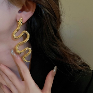 Close-up of golden snake drop earring with green gemstone eye on model's ear