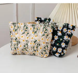 Detail of embroidered daisy pouches in beige and black fabric with secure zipper closure
