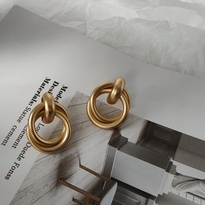 Detail of matte gold double-hoop knotted earrings on a minimalist fashion magazine