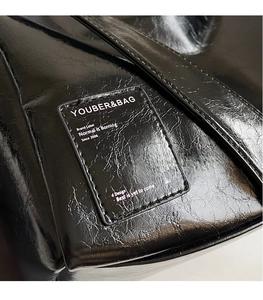 Close-up of black wrinkled oil wax leather texture and logo patch on the Boston bag
