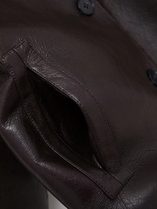 Detail of dark brown leather jacket showing grain texture, side pocket and black buttons