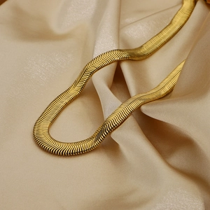 Dettaglio macro della collana a catena piatta dorata su seta color champagne
