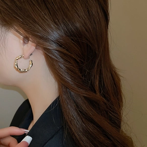 Detail of gold C-shaped twisted hoop earrings with small diamonds on a model