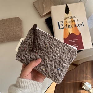 Close-up of brown herringbone wool mini pouch featuring a zipper and a fabric brand label