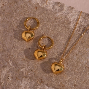 Golden stainless steel jewelry set featuring 3D heart pendants and hoop earrings on stone